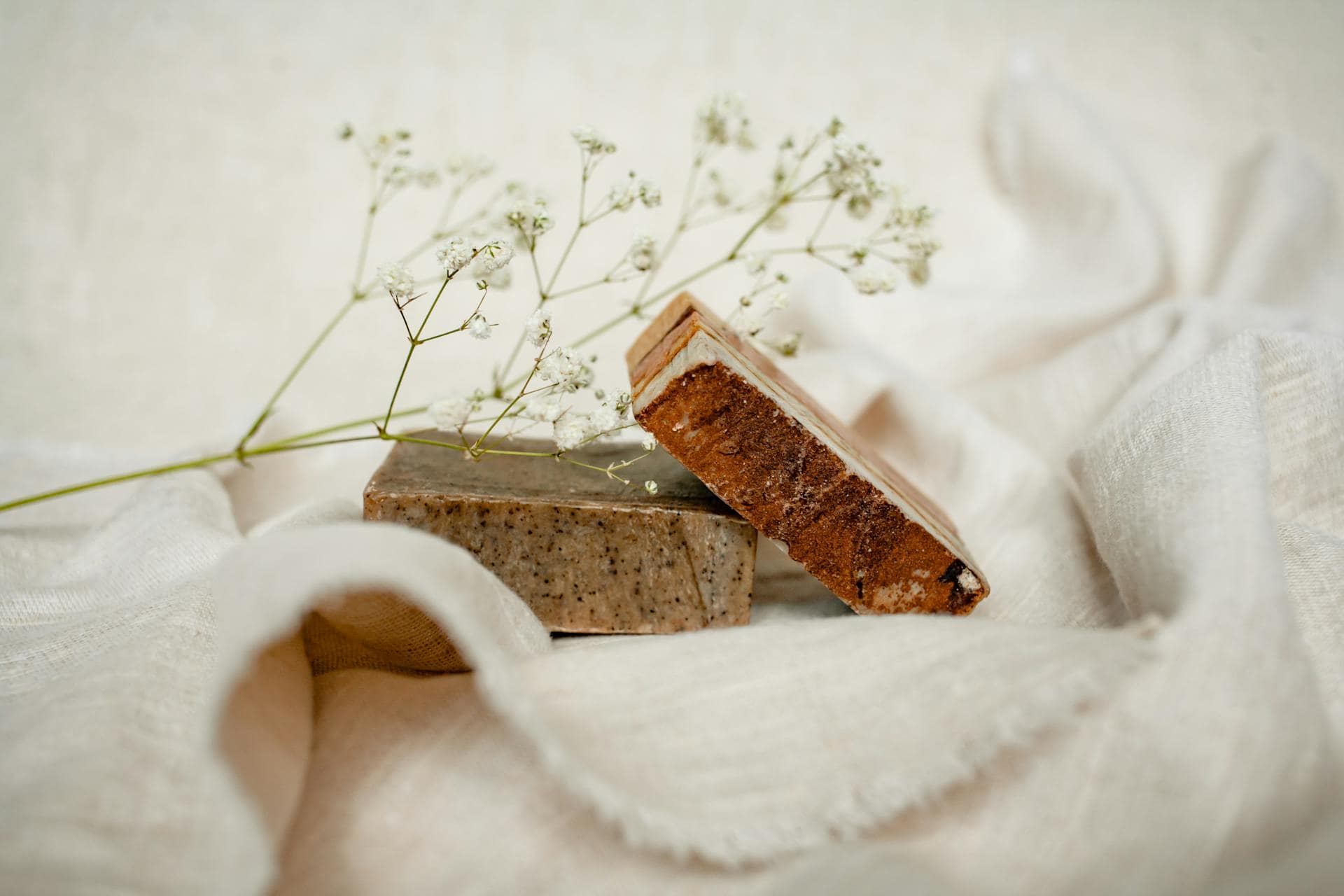 Two handmade soap bars with a delicate white flower on a soft fabric