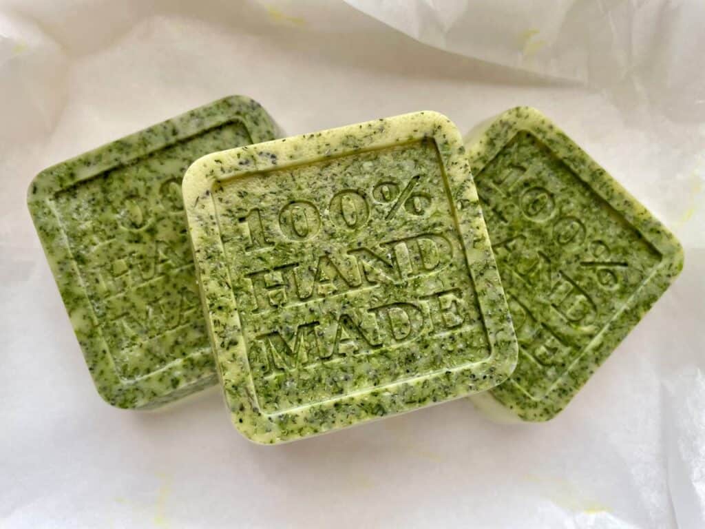 Three green square soap bars with “100% HAND MADE” stamped on top